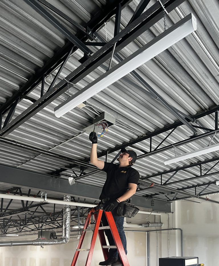 electrician installing overhead lighting in a commercial space